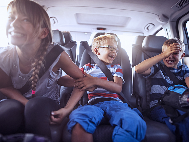 Happy playful kids sitting in the back of car on road trip