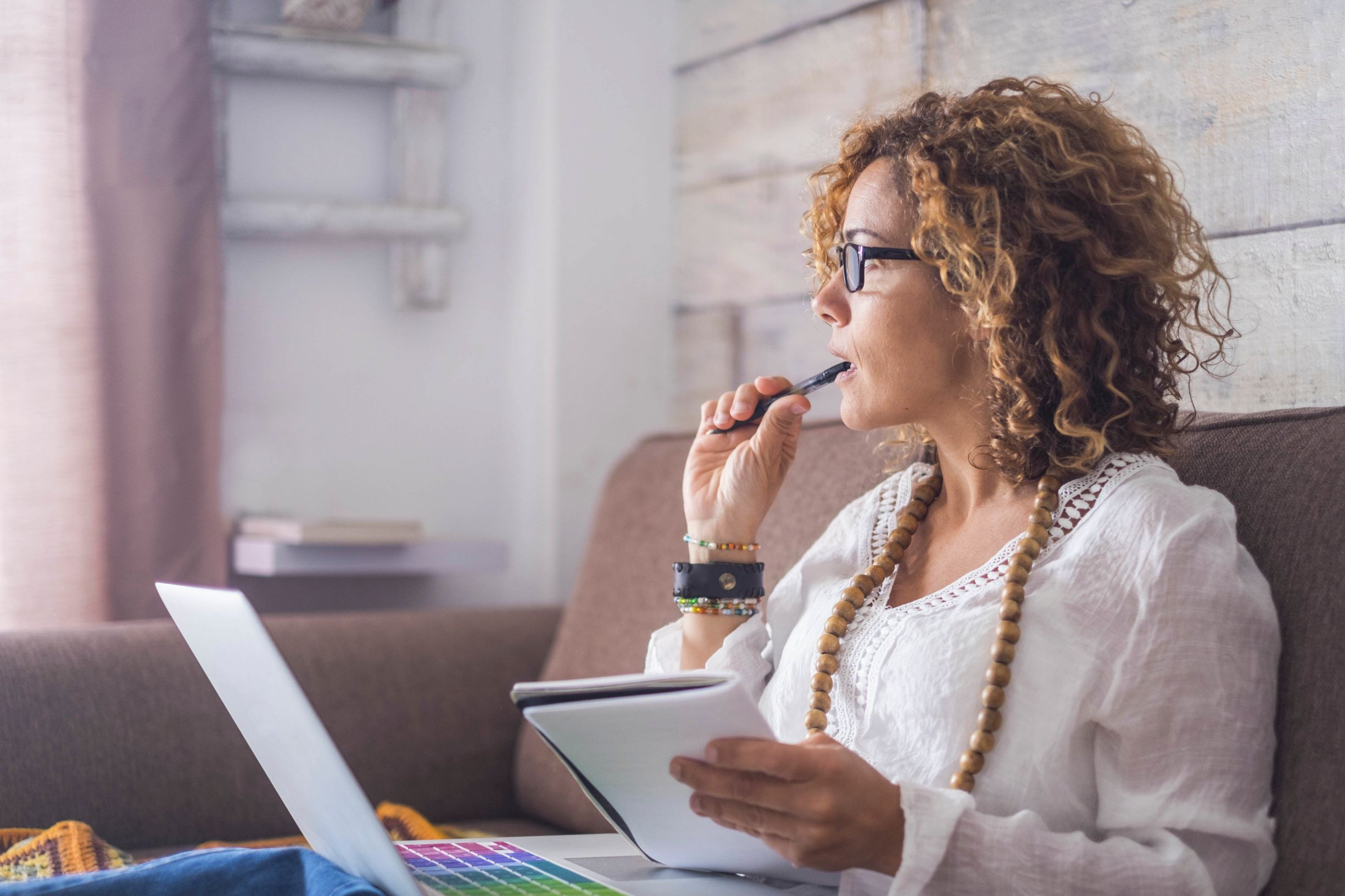 Portrait of thoughtful woman sitting on sofa with a laptop on her lap