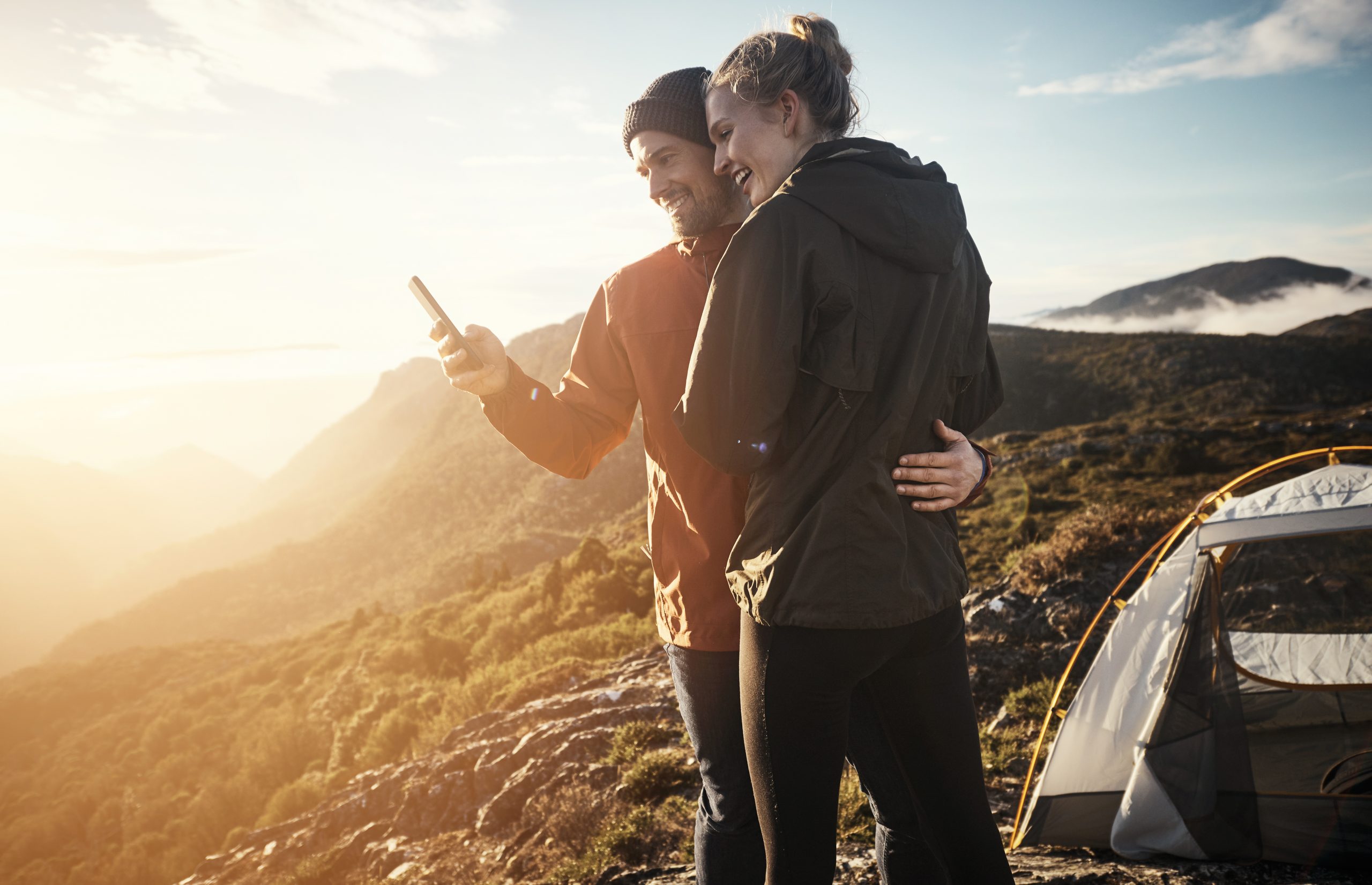 Young couple using a smartphone by their tent while camping in the mountains