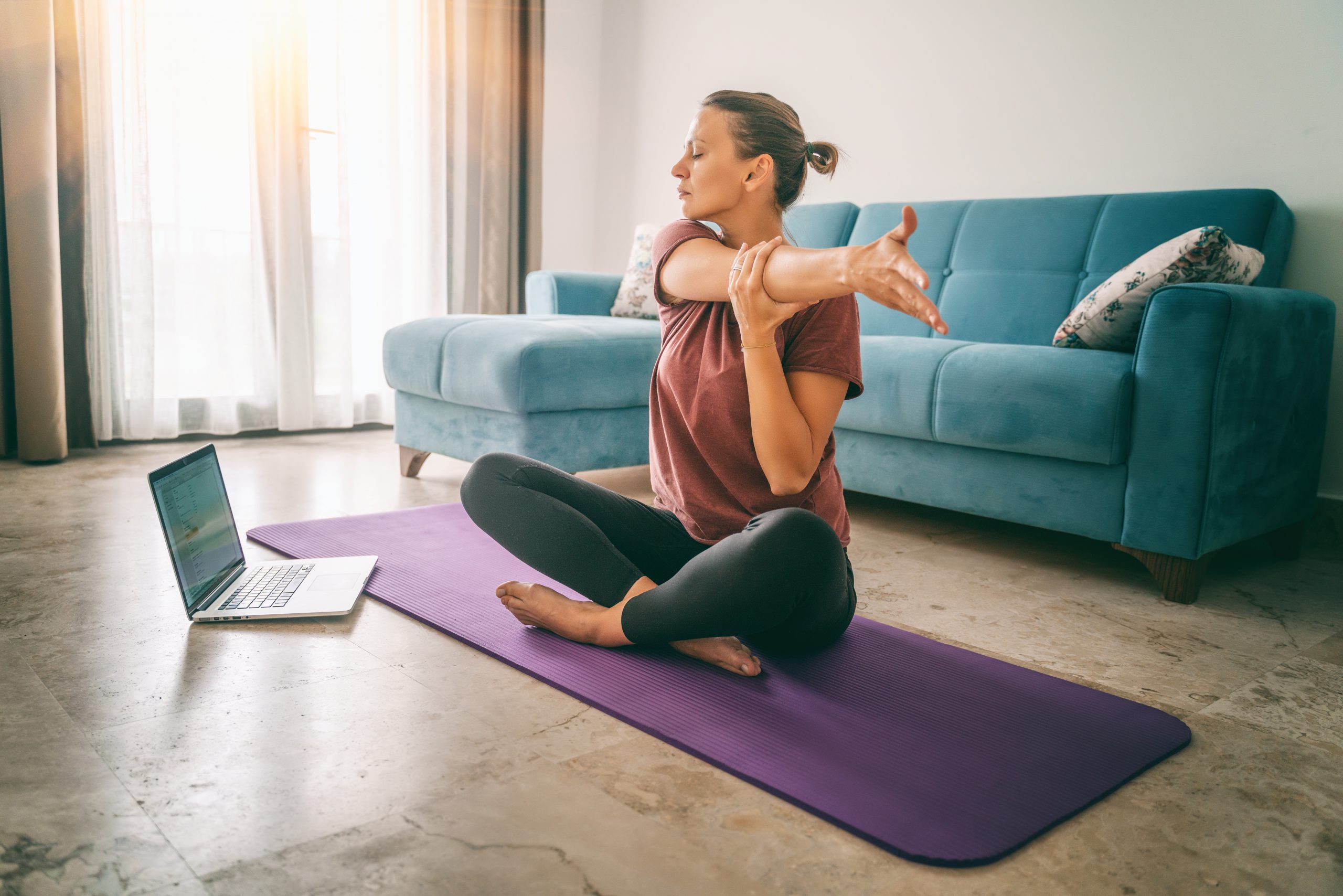 Women doing yoga on mat with laptop next to her