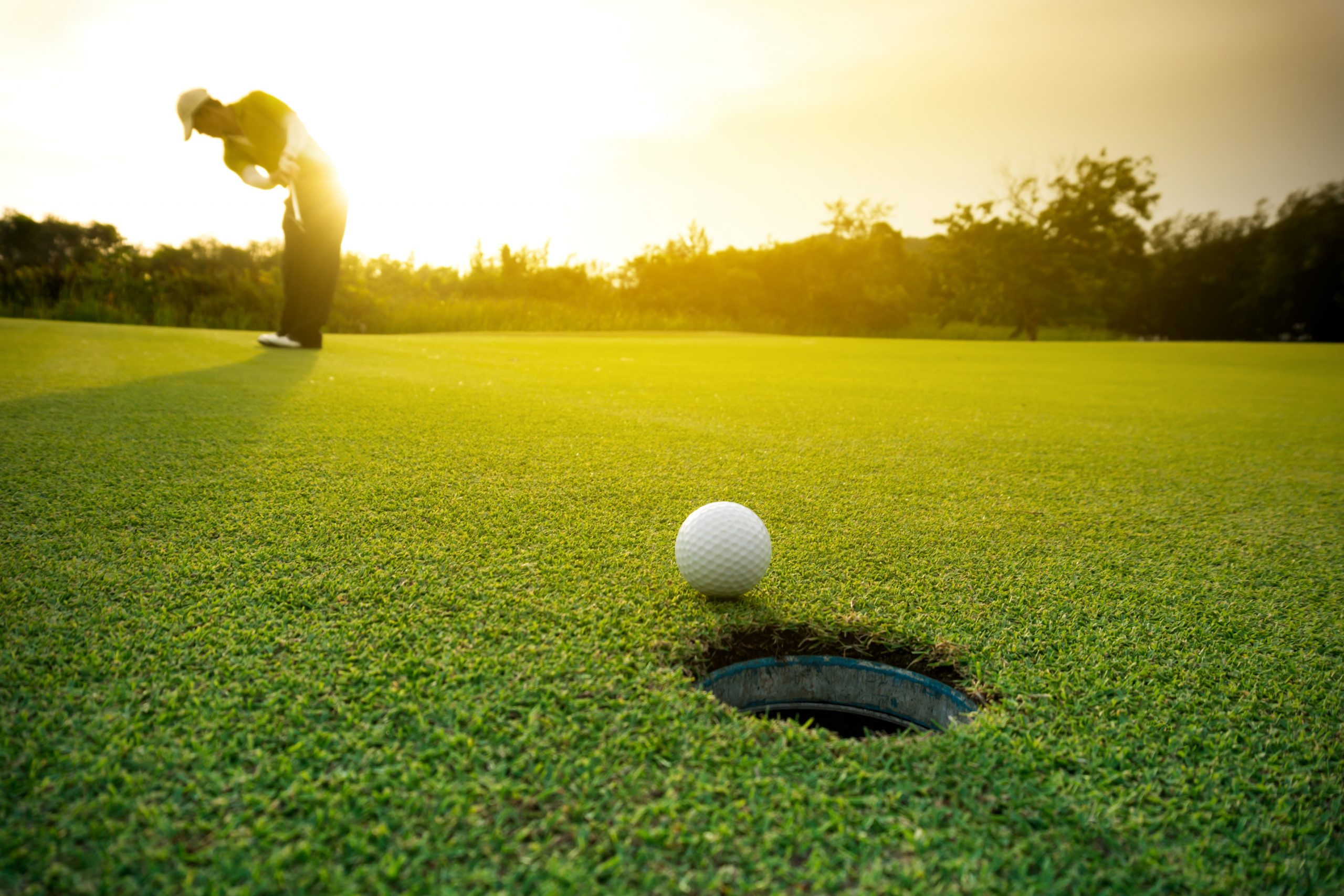 Closeup of while golf ball ear hole with golf player in the background