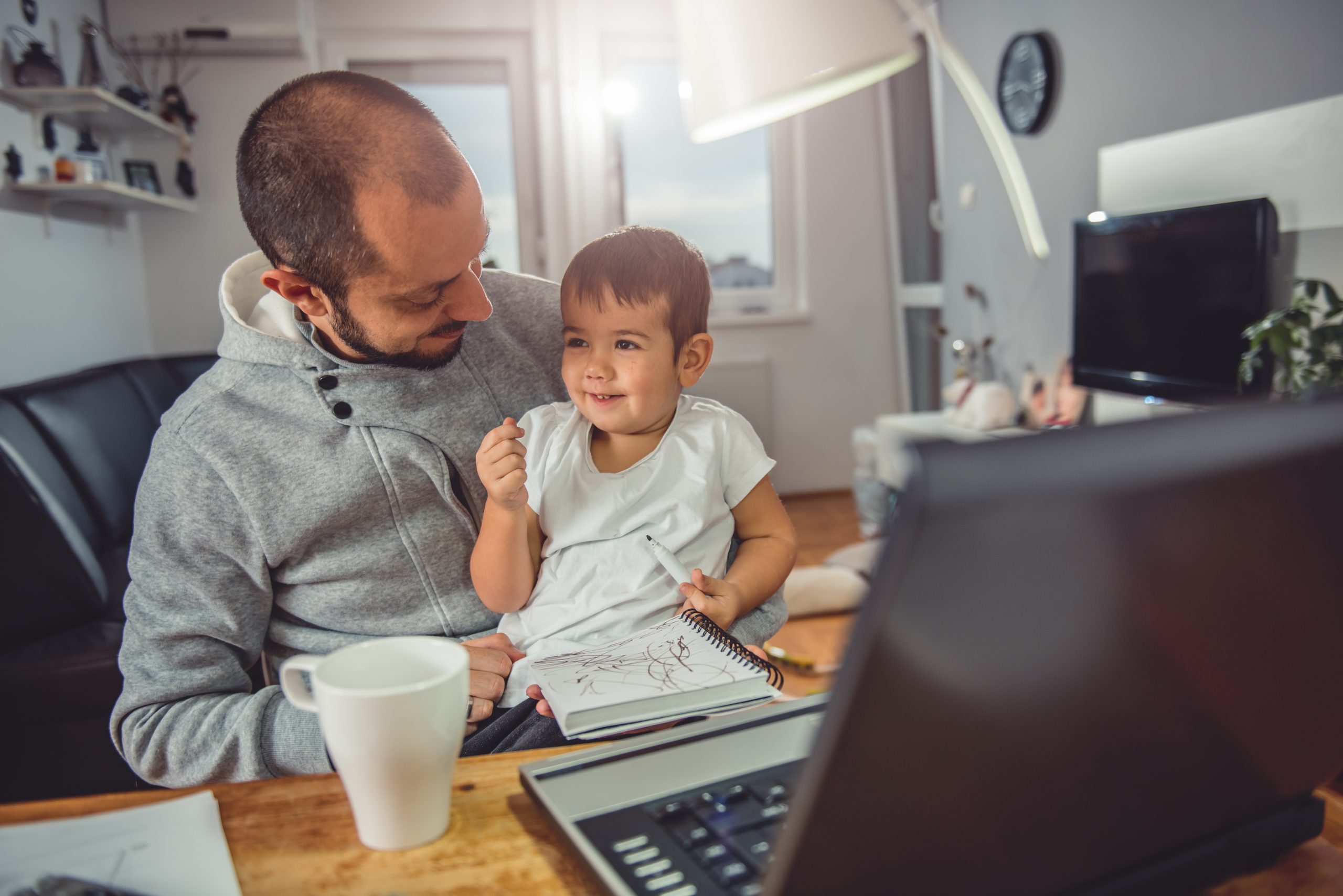 Happy dad with daughter on his lap sitting at table in front of laptop